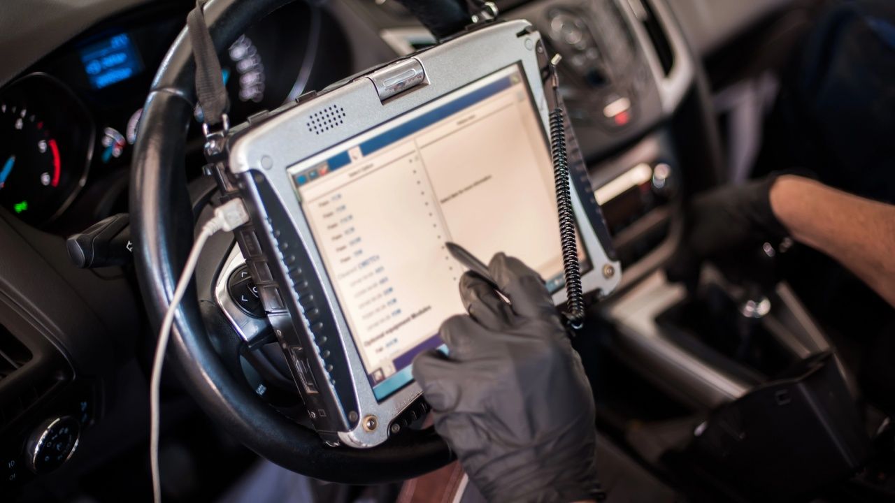 Mecánico consulta datos en la pantalla de un dispositivo OBD2 conectado a un vehículo.