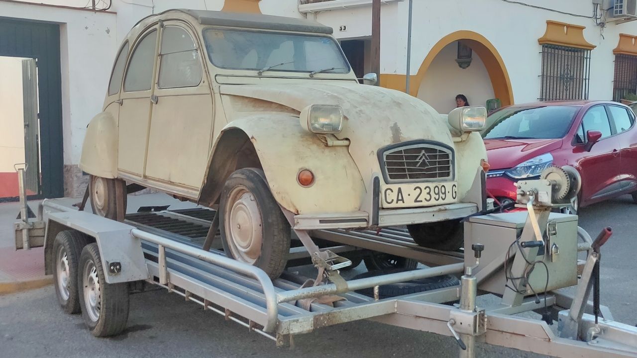 Un Citroën 2CV blanco en muy mal estado subido a un remolque.