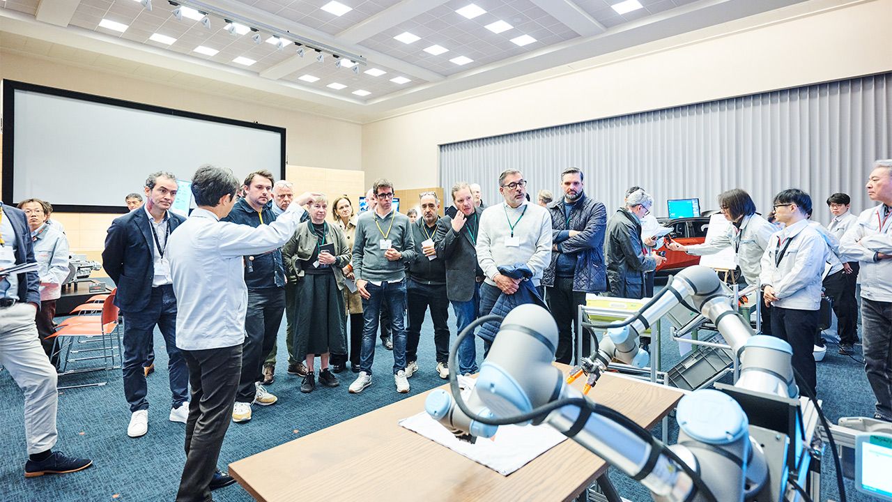 Brazos robóticos colaborativos sobre una mesa y un grupo de asistentes en una sala durante un evento de Toyota