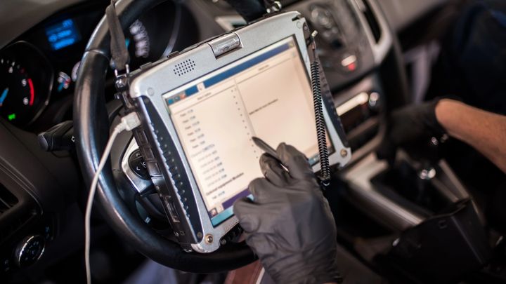 Mecánico consulta datos en la pantalla de un dispositivo OBD2 conectado a un vehículo.